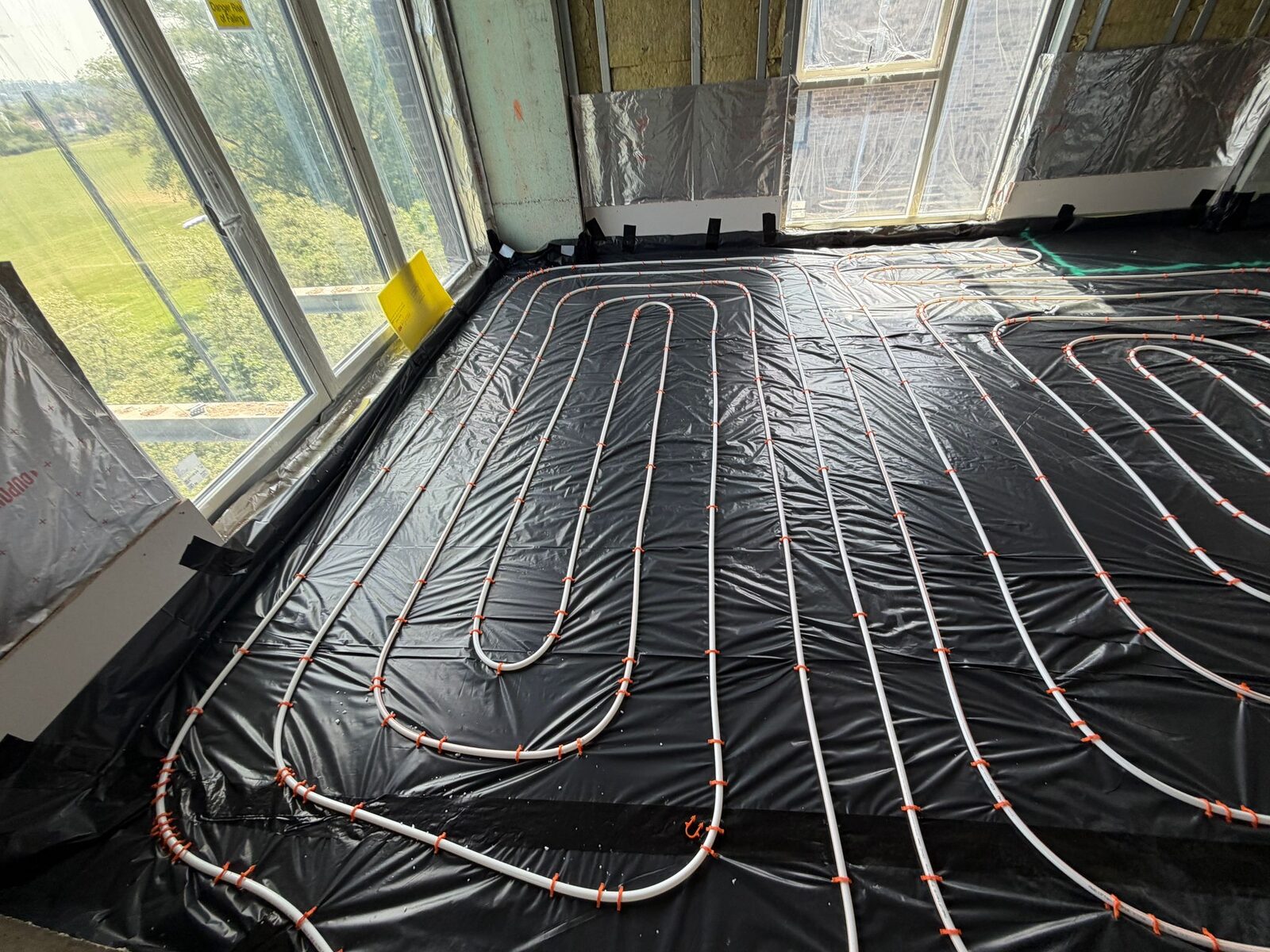 Low-profile wet underfloor heating being installed across a bright room in an existing London home